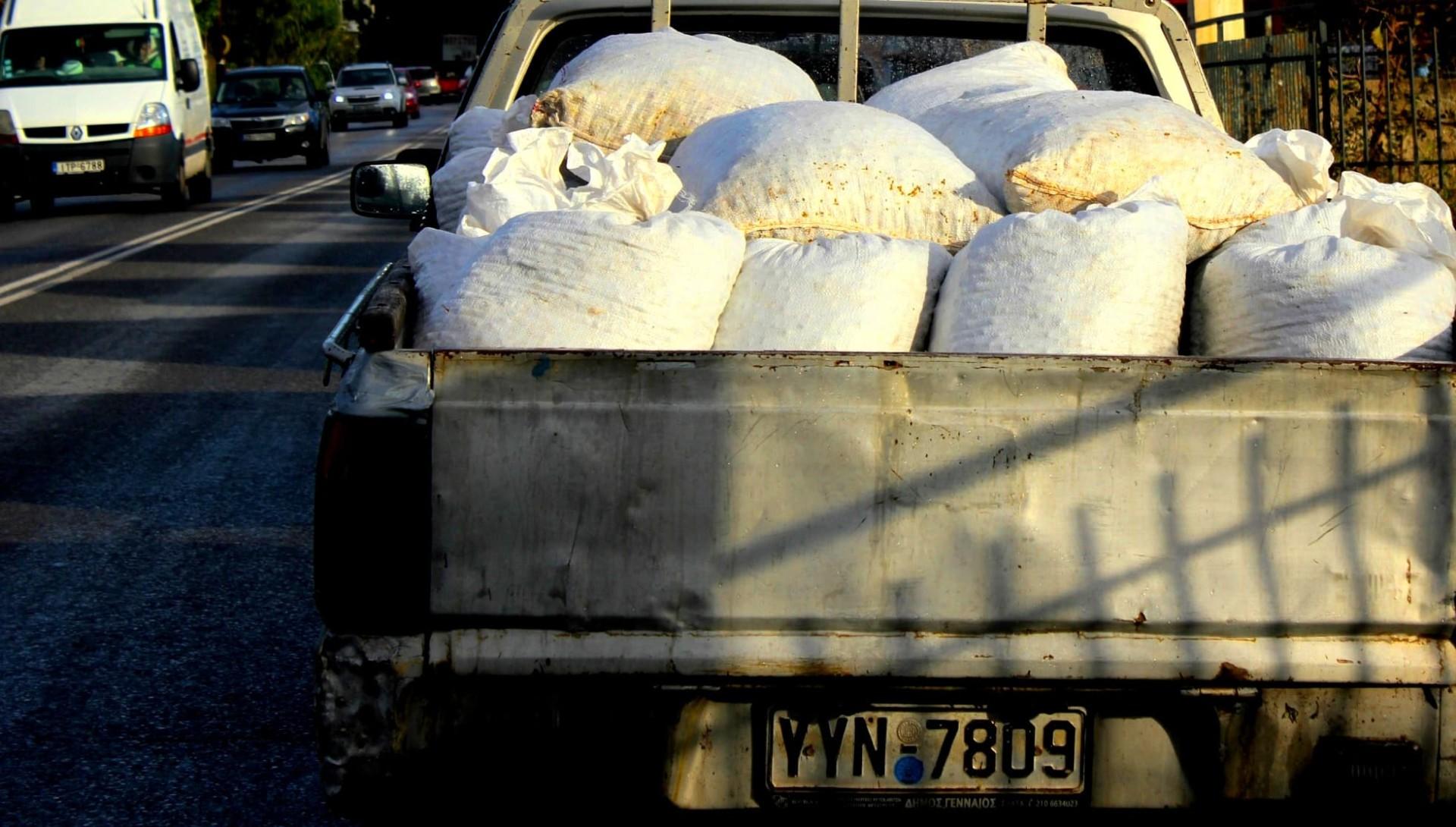 Pickup truck with a bed full of white bags on a street. - Olive Oil Times