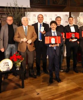 A group of individuals posing with awards during a ceremony, featuring various trophies and certificates. - Olive Oil Times
