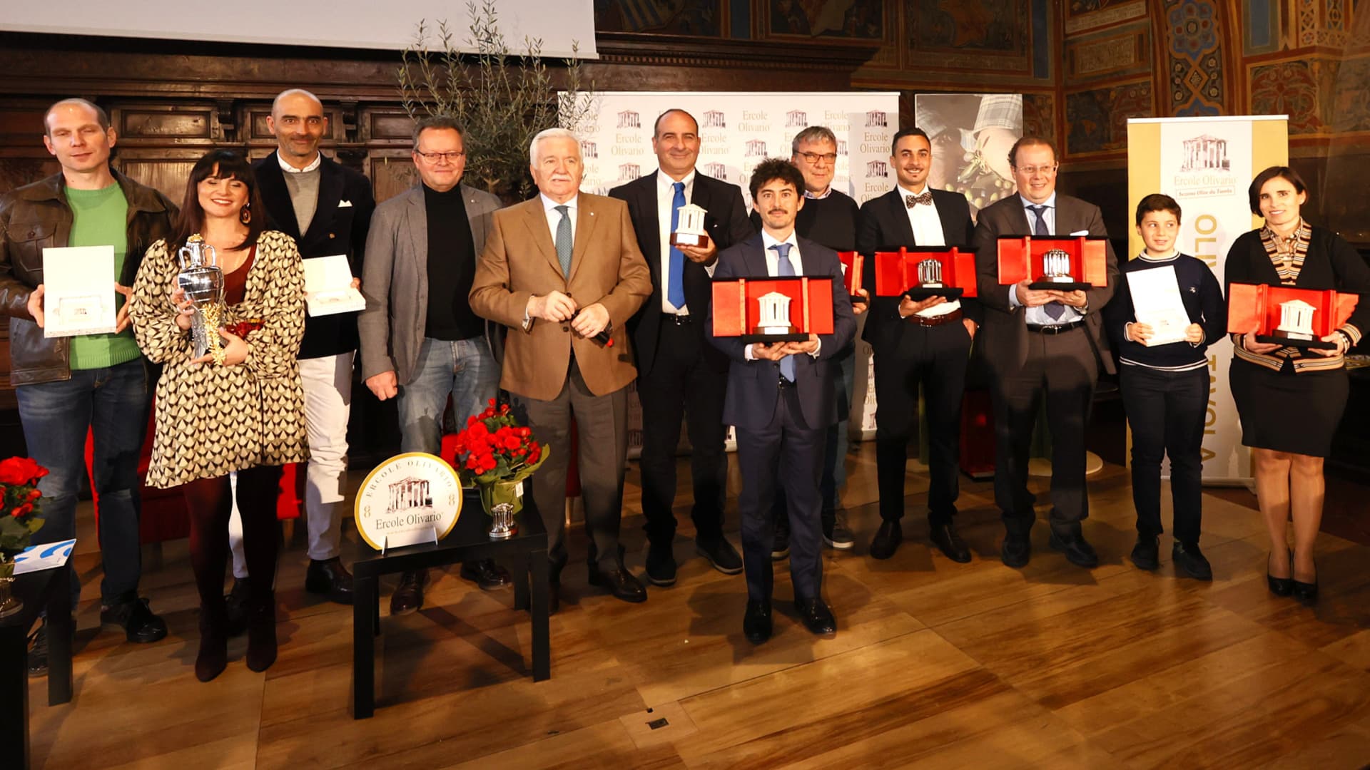 A group of individuals posing with awards during a ceremony, featuring various trophies and certificates. - Olive Oil Times