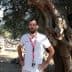 A man wearing a white shirt and lanyard standing beside a large olive tree. - Olive Oil Times