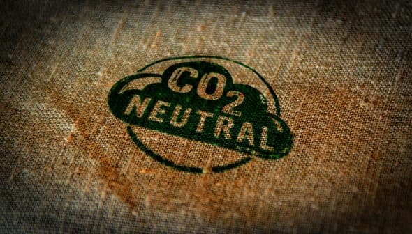 Green CO2 neutral stamp printed on a textured fabric background. - Olive Oil Times
