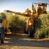 A yellow olive harvesting machine and a blue tractor in an olive grove during harvest season. - Olive Oil Times