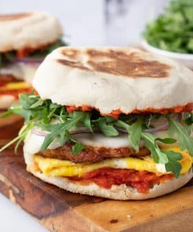 Breakfast sandwich featuring a fried egg, sausage patty, and fresh greens on a toasted bun. - Olive Oil Times