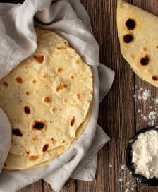 A stack of freshly made flatbreads wrapped in a cloth with flour and oil on a wooden surface. - Olive Oil Times