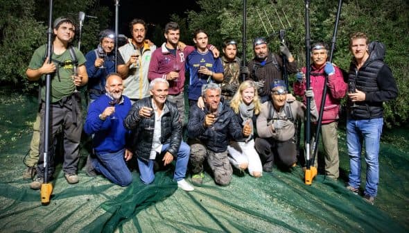 Group of individuals posing together with olive harvesting tools during nighttime. - Olive Oil Times