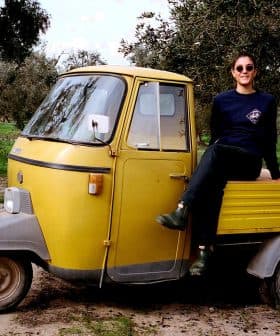 A person sitting on a yellow three-wheeled vehicle in an outdoor setting with trees. - Olive Oil Times