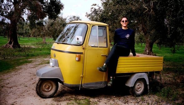 A person sitting on a yellow three-wheeled vehicle in an outdoor setting with trees. - Olive Oil Times