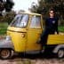 A person sitting on a yellow three-wheeled vehicle in an outdoor setting with trees. - Olive Oil Times