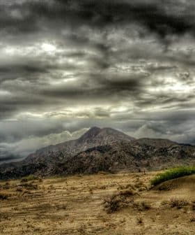 A mountain range under a dramatic cloudy sky with dark clouds and a barren landscape in the foreground. - Olive Oil Times
