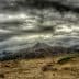 A mountain range under a dramatic cloudy sky with dark clouds and a barren landscape in the foreground. - Olive Oil Times