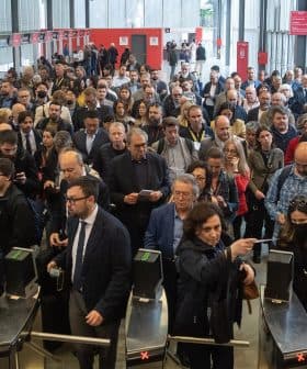 Large crowd of people waiting in line at an event entrance with ticket barriers. - Olive Oil Times
