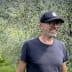 Man wearing a black cap and glasses smiling while standing in an olive grove. - Olive Oil Times