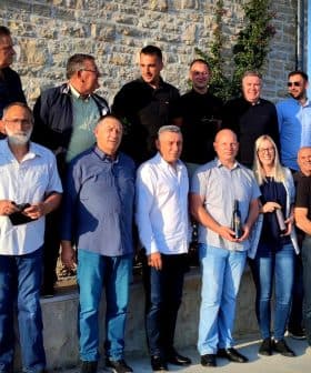 A group of individuals posing together outdoors in a casual setting, some holding bottles. - Olive Oil Times