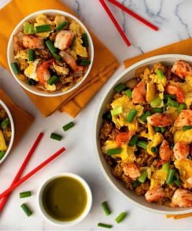 A serving of shrimp fried rice topped with green onions in a skillet and two bowls. - Olive Oil Times