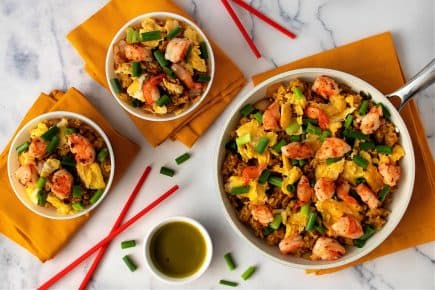A serving of shrimp fried rice topped with green onions in a skillet and two bowls. - Olive Oil Times