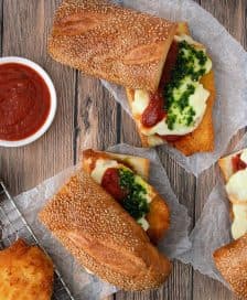 Two Italian sandwiches filled with fried chicken, cheese, and sauces on a wooden surface. - Olive Oil Times