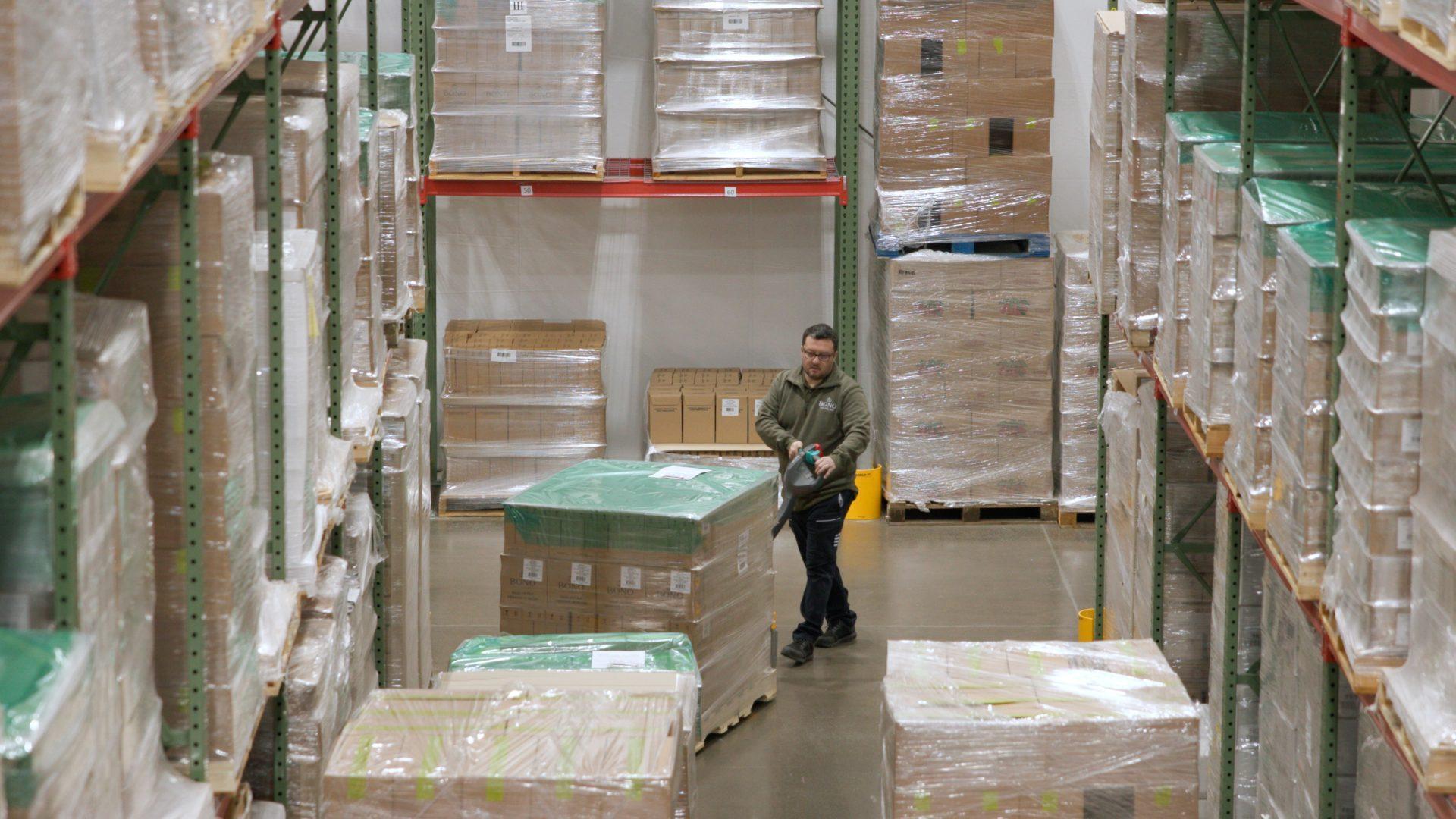 Warehouse worker using a pallet jack to move a large pallet in a storage facility. - Olive Oil Times