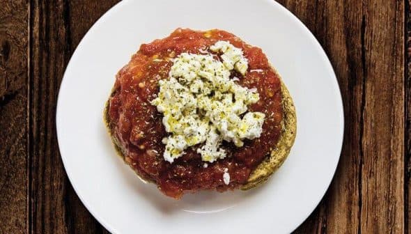 A plate of dakos salad featuring a base of barley rusk topped with tomato sauce and crumbled feta cheese. - Olive Oil Times
