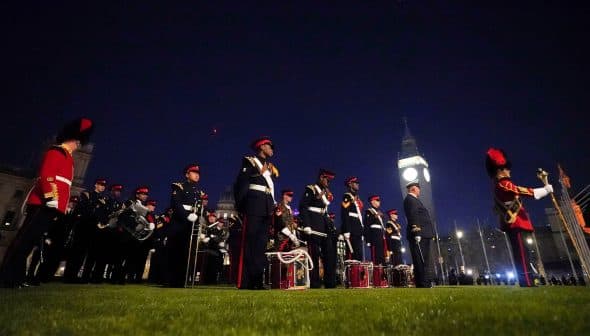 A group of ceremonial guards in uniform standing in formation at night with Big Ben in the background. - Olive Oil Times