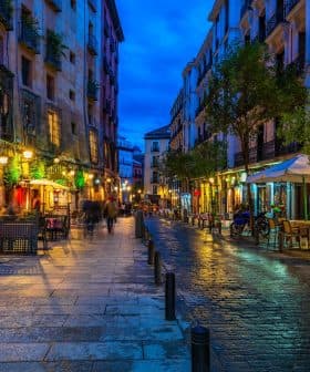 Narrow street in a European city illuminated by lights with outdoor dining areas and wet cobblestones. - Olive Oil Times