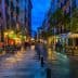 Narrow street in a European city illuminated by lights with outdoor dining areas and wet cobblestones. - Olive Oil Times