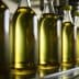 Row of glass bottles filled with olive oil on a production line in a factory setting. - Olive Oil Times