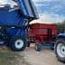 New Holland olive harvester unloading olives into a red trailer attached to a blue tractor. - Olive Oil Times
