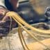A hand holding freshly rolled pasta strands from a pasta machine in a kitchen setting. - Olive Oil Times