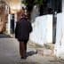 An elderly man walking away on a cobblestone street lined with buildings and greenery. - Olive Oil Times