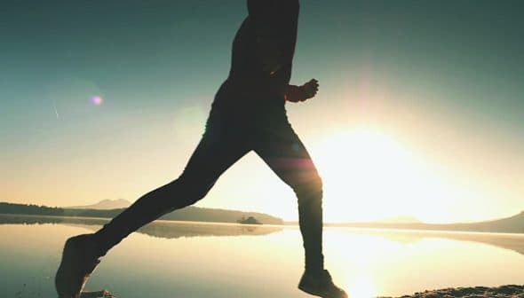 Silhouette of a person jogging along the shore of a lake during sunrise. - Olive Oil Times