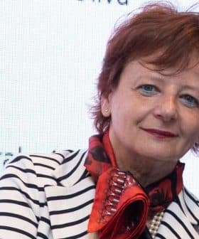 Woman with short red hair wearing a striped blazer and a red scarf, posing for the camera. - Olive Oil Times