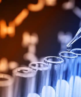 A pipette dropping liquid into a row of test tubes with a blurred clock in the background. - Olive Oil Times