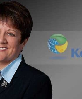 A business executive in a black suit with a light blue shirt, smiling against a dark background with the KeHE logo. - Olive Oil Times