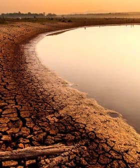 Dry, cracked earth along the edge of a river reflecting the sunset light. - Olive Oil Times