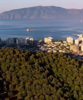 Aerial view of a coastal city with buildings and mountains in the background. - Olive Oil Times