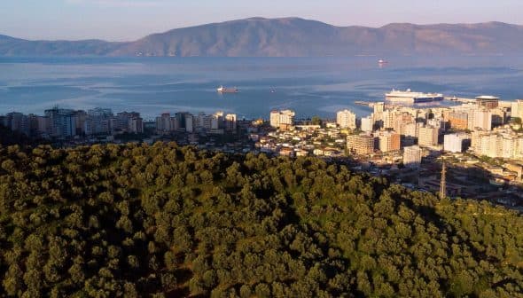 Aerial view of a coastal city with buildings and mountains in the background. - Olive Oil Times