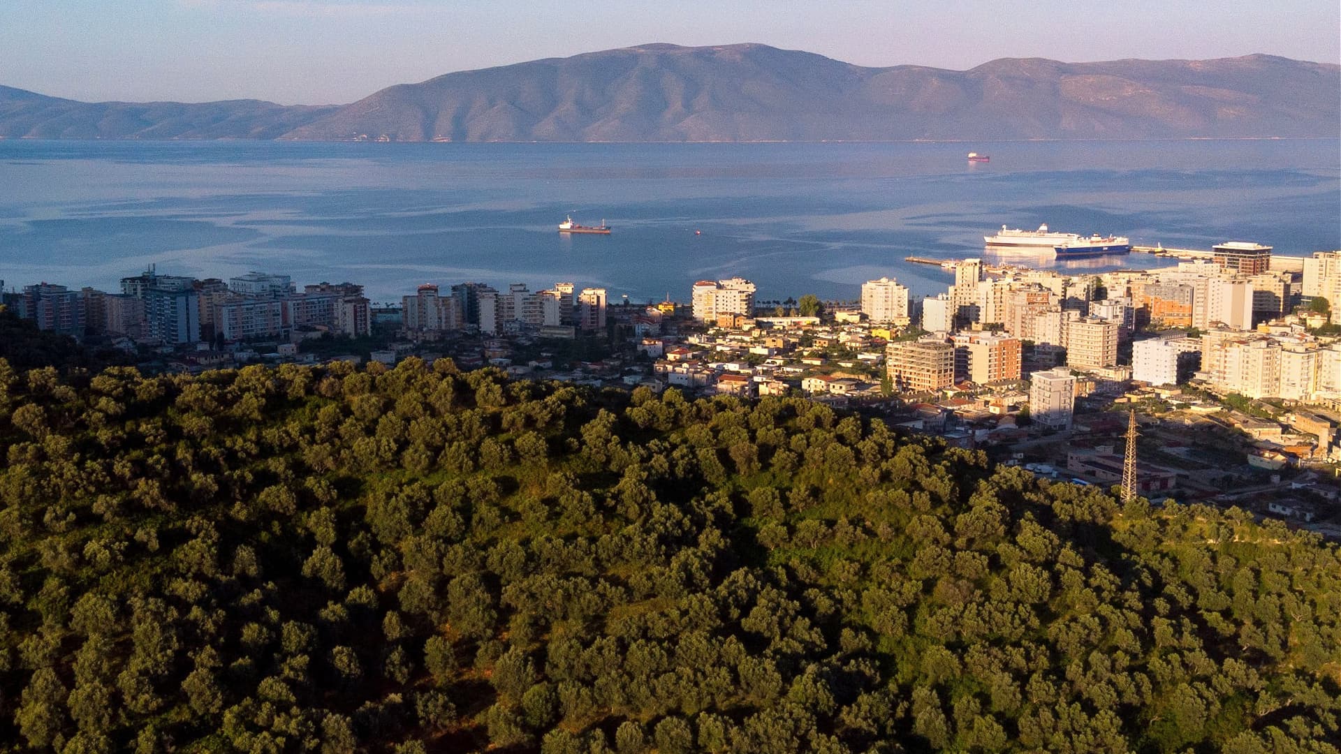 Aerial view of a coastal city with buildings and mountains in the background. - Olive Oil Times