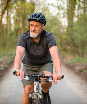 Older man wearing a helmet riding a bicycle on a forest trail during daylight. - Olive Oil Times