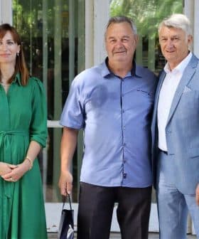 Three individuals standing together for a photo, with one woman in a green dress and two men in casual and formal attire. - Olive Oil Times
