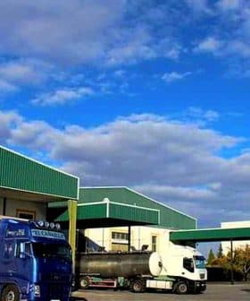 Dcoop warehouse building with two trucks parked in front under a blue sky. - Olive Oil Times