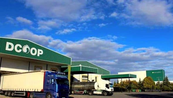Dcoop warehouse building with two trucks parked in front under a blue sky. - Olive Oil Times