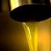 Golden olive oil flowing from a metal tap into a container in a close-up view. - Olive Oil Times