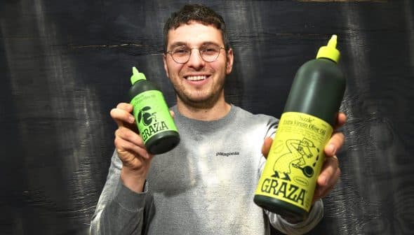 Person holding two bottles of Grazia extra virgin olive oil, one large and one small, both with green labels. - Olive Oil Times