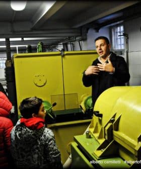 A man explaining olive oil production to a group of people in a mill setting. - Olive Oil Times