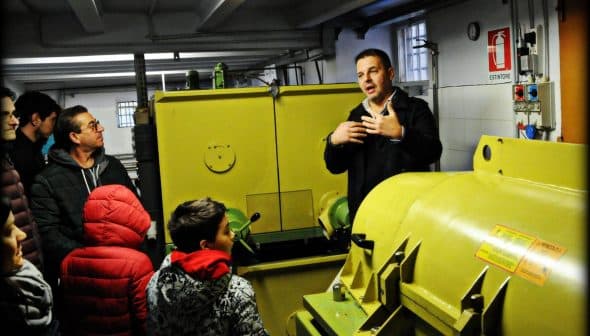 A man explaining olive oil production to a group of people in a mill setting. - Olive Oil Times
