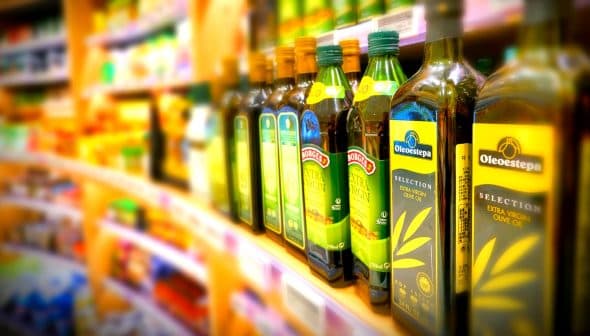 Various bottles of olive oil displayed on a store shelf in a grocery aisle. - Olive Oil Times