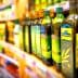 Various bottles of olive oil displayed on a store shelf in a grocery aisle. - Olive Oil Times