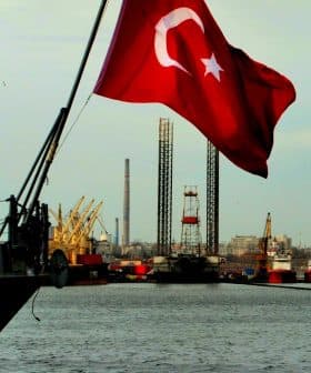 Turkish flag waving on a ship with cranes and industrial structures in the background. - Olive Oil Times