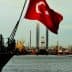 Turkish flag waving on a ship with cranes and industrial structures in the background. - Olive Oil Times