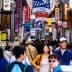 Crowd of people walking through a bustling street market filled with colorful signs in Japan. - Olive Oil Times
